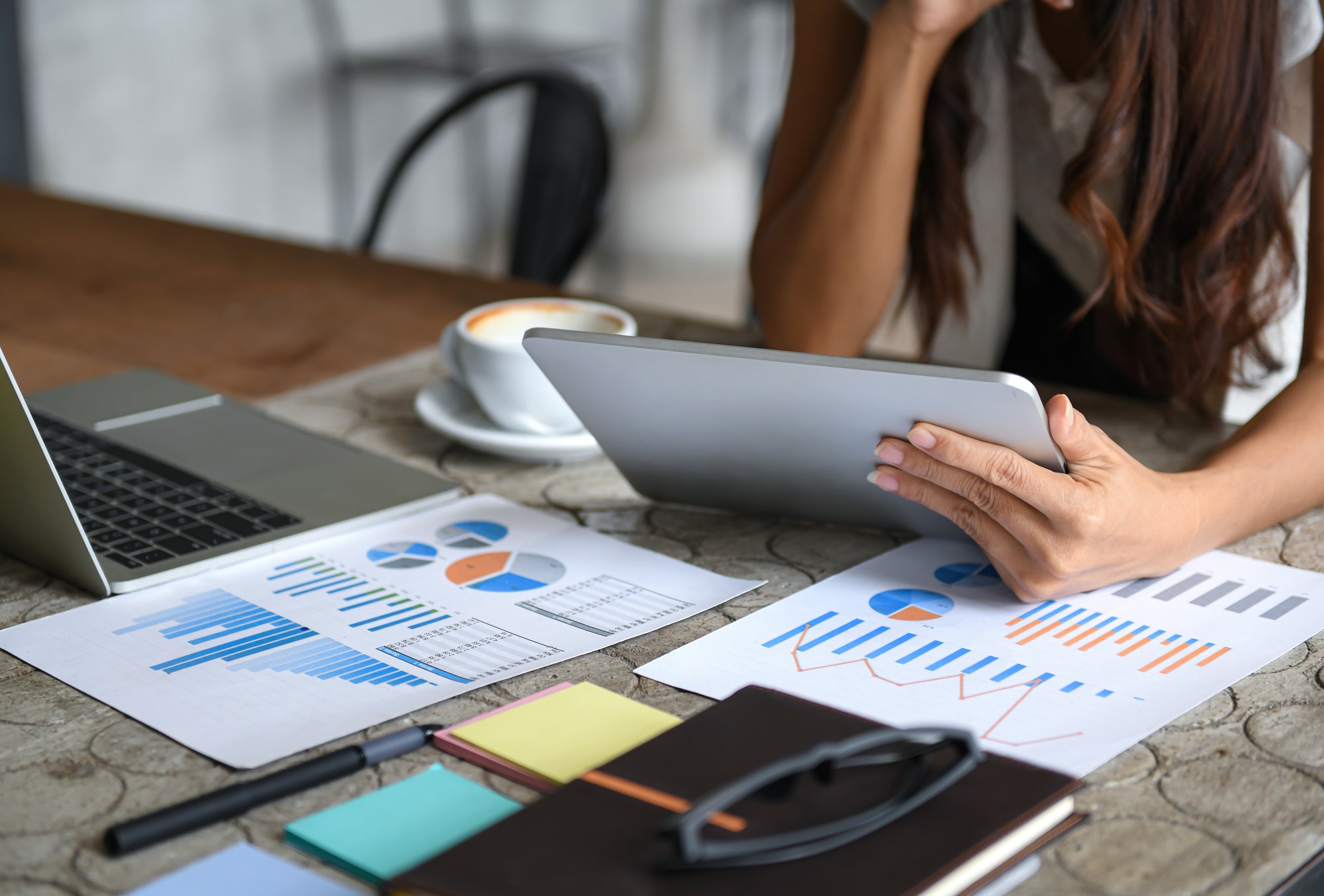 Female businessmen are using the tablet during leisure. Graphs, documents placed on the table.