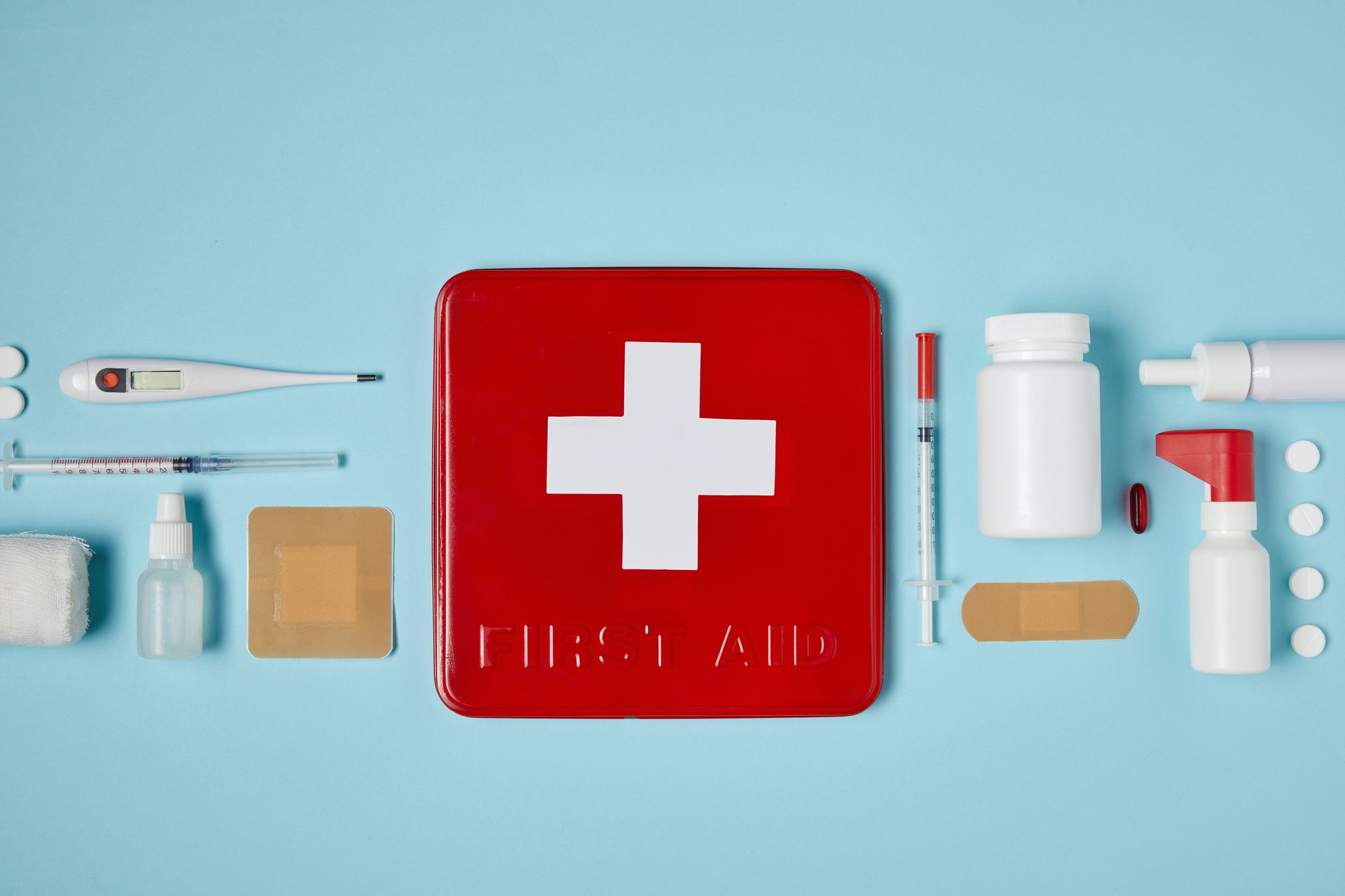 top view of red first aid kit box on blue surface with medical supplies